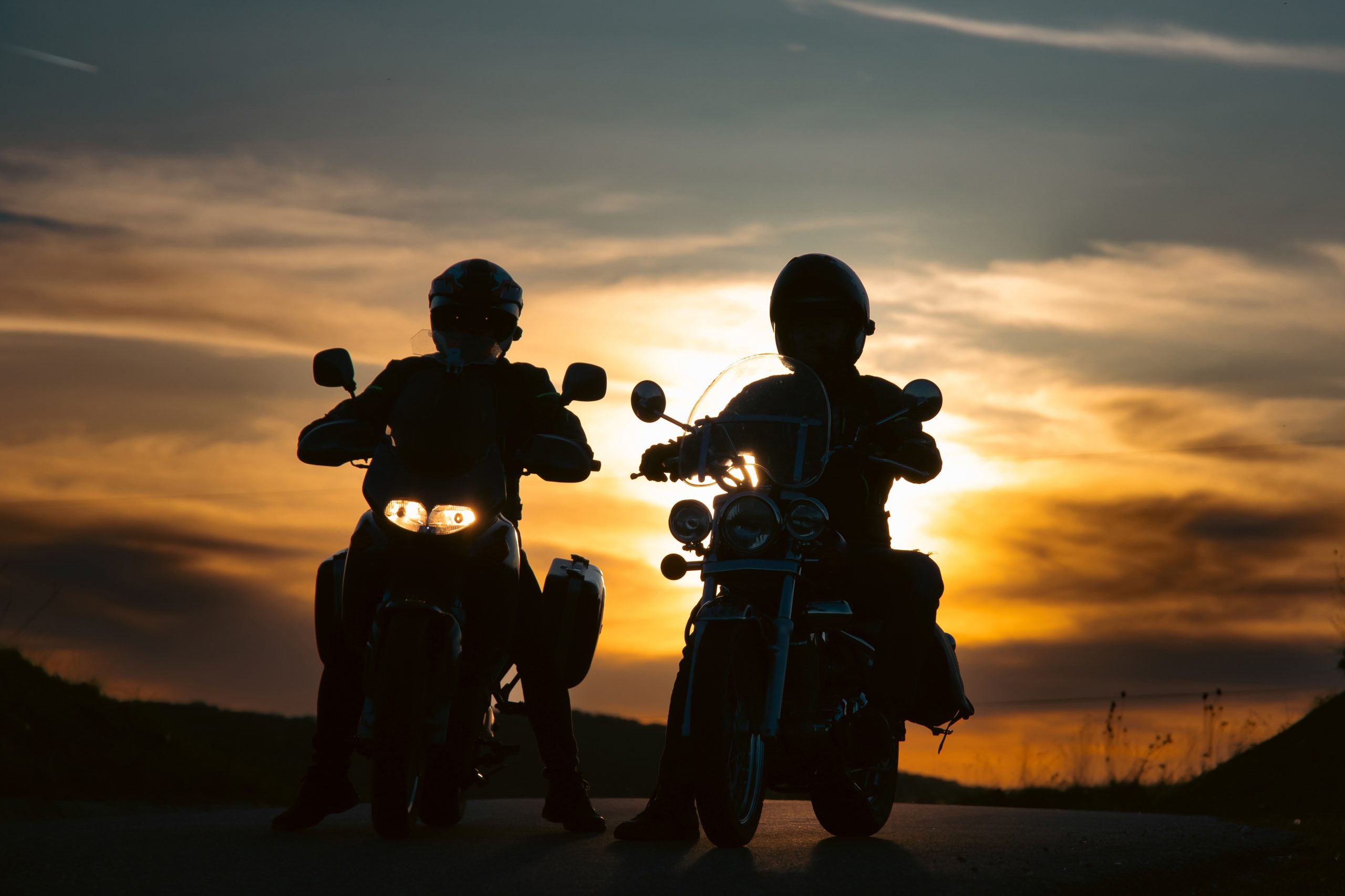 Silhouette,Of,Two,Motorcycle,Riders,On,The,Road,With,Sunset
